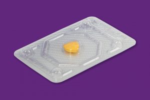 Photo d'une pilule du lendemain prise dans son emballage. L'emballe est de couleur grise, en aluminium et la pilule et de couleur jaune.