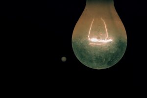 Photo d'une ampoule avec un arrière plan noir dans laquelle on voit un filament de lumière allumé à l'intérieur de celle-ci
