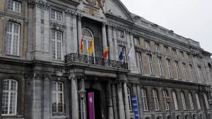 Photo de l'entrée du Palais de Justice de la Ville de Liège. L'entrée est ornée de piliers en brique grise. Sur le balcon du batiment, il y a 5 drapeaux: en partant de la gauche, le drapeau de la province de Liège, le drapeau de la Région Wallonne, le drapeau de la Belgique, le drapeau de l'Union Européenne et le drapeau de la communauté française