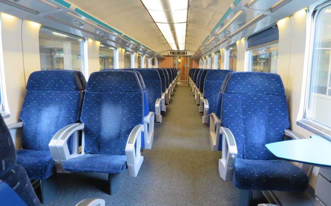 Photo d'un wagon de 1ère classe de la SNCB prise au milieu de l'allée centrale. Les sièges sont bleus avec des motifs vers et rouges.