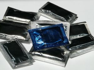 Photo de préservatifs posés sur une table blanche. Tous les préservatifs sont emballés dans des sachets gris sauf un, qui se trouve au dessus de tous les autres, qui est de couleur bleue.