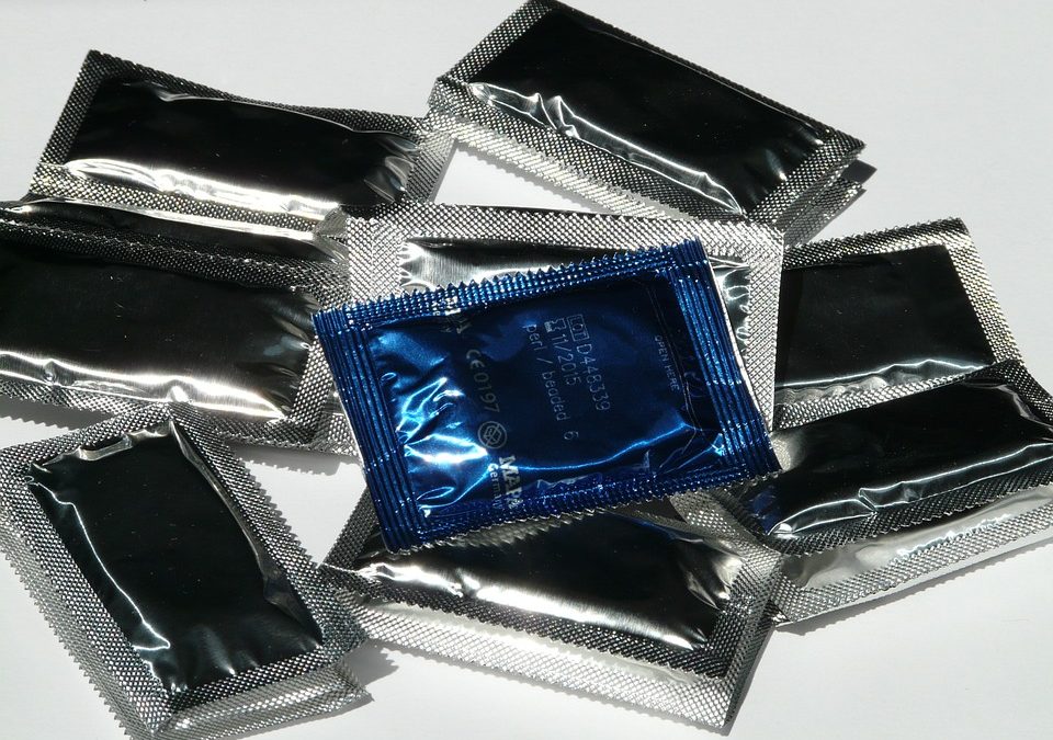 Photo de préservatifs posés sur une table blanche. Tous les préservatifs sont emballés dans des sachets gris sauf un, qui se trouve au dessus de tous les autres, qui est de couleur bleue.