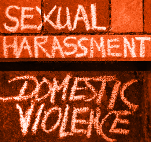 Photo d’un mur en brique rouge sur lequel est écrit à la craie blanche « Sexual Harassment» et en dessous : « Domestic violence».