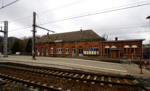 Photo de la gare de Vivegnis sur laquelle il y a un bâtiment en arrière-plan. En avant plan une ligne de chemin de fer avec les quais sur lesquels peuvent se rendre les passagers.